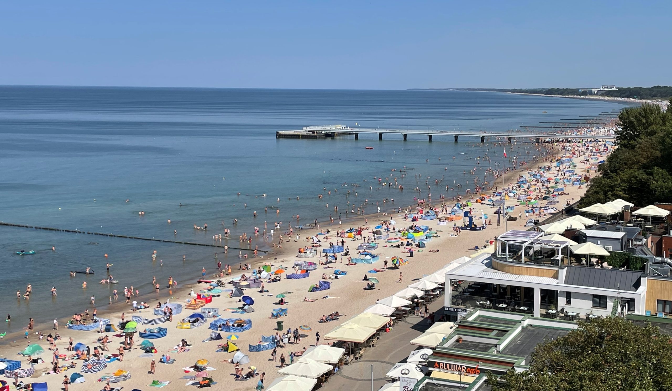 widok na morze i plażę w Kołobrzegu, na plaży leżą ludzie, w morzu się kąpią