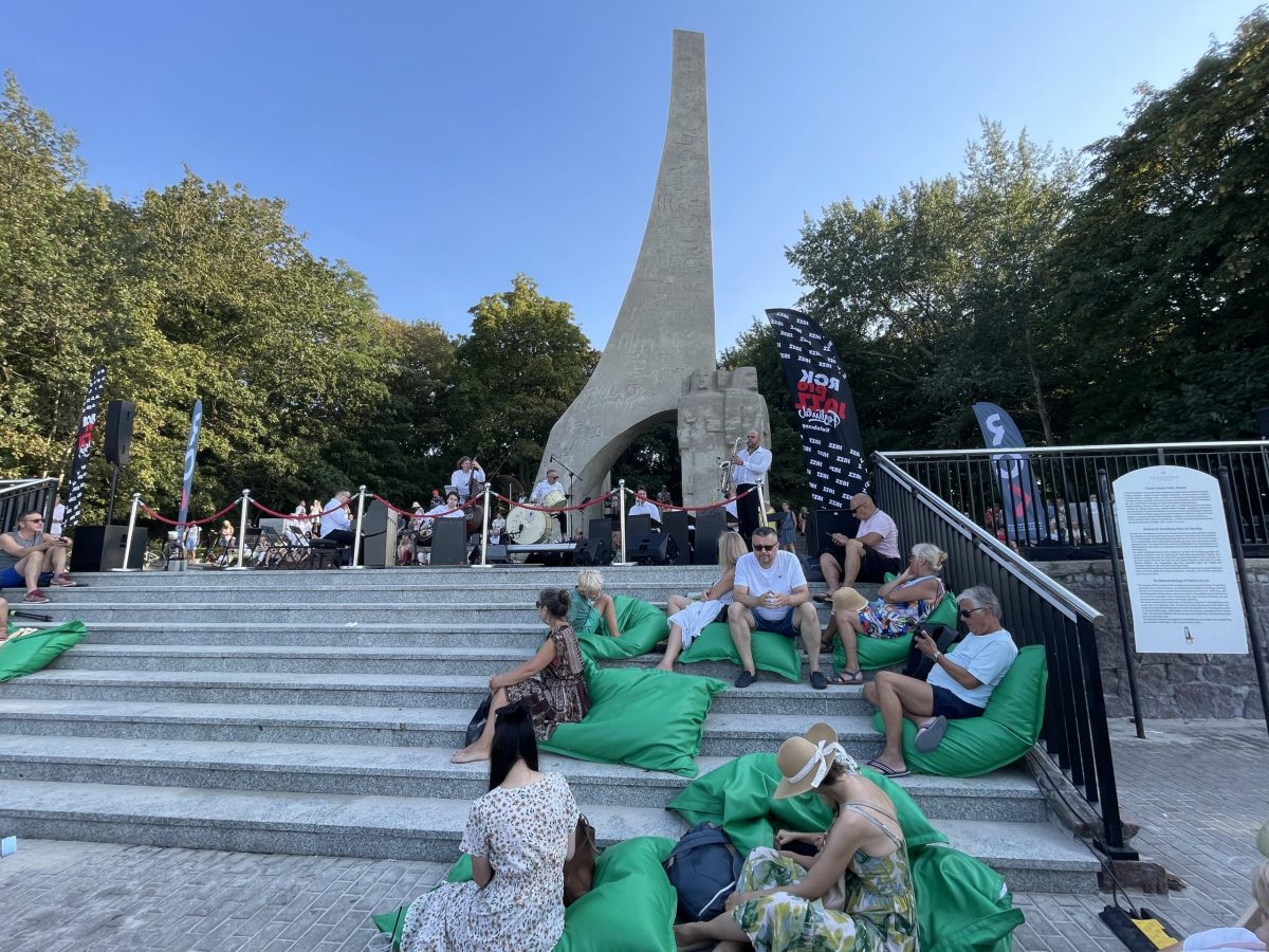 ludzie siedzą pod pomnikiem Zaslubin w Kołobrzegu