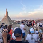 na zjdęciu ludzie na plaży, w tle zamek z piasku